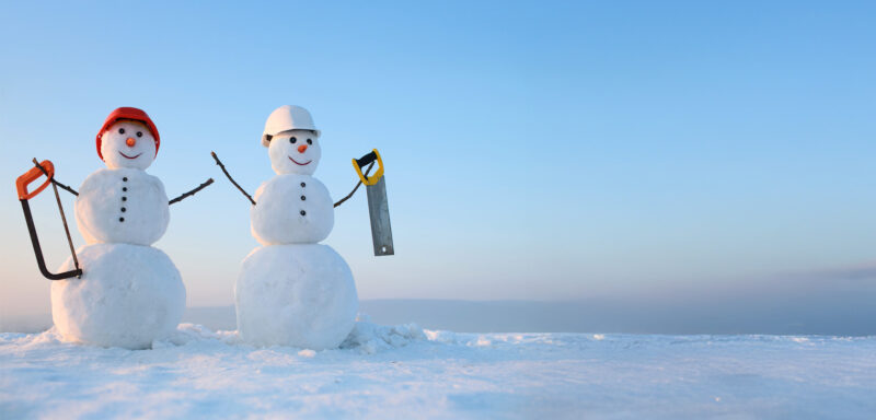 Kuvassa kaksi rakennusmies-lumiukkoa kypärät päässä ja sahat kädessä.