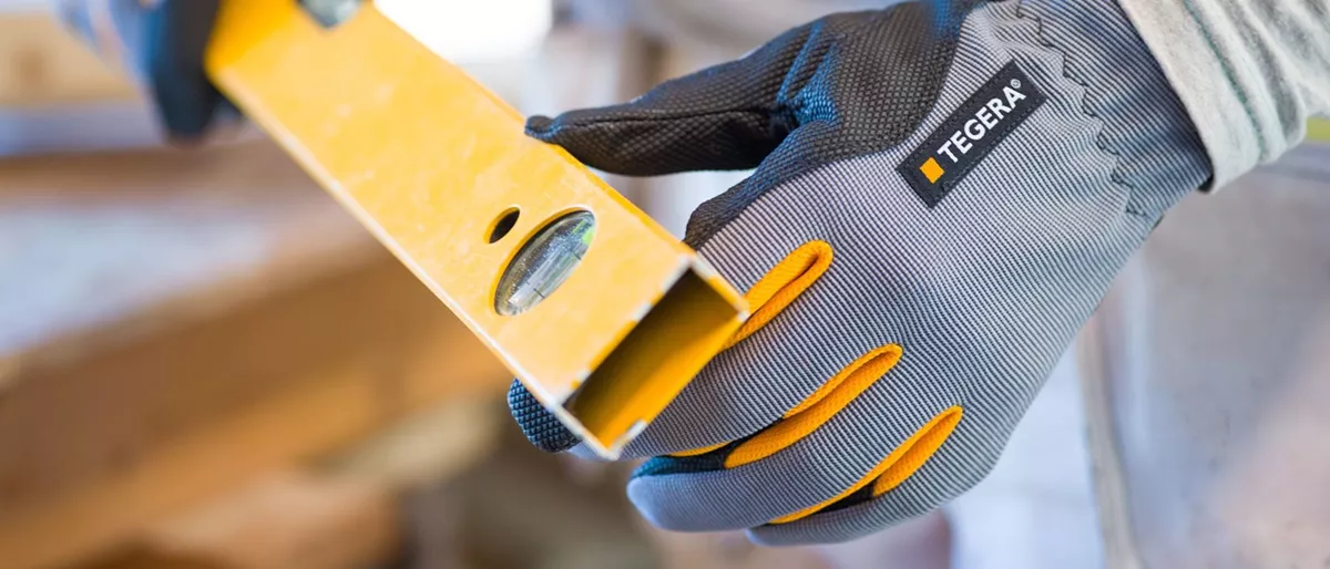 Kuvassa TEGERA-hansikkaalla suojattu käsi pitelee vatupassia.